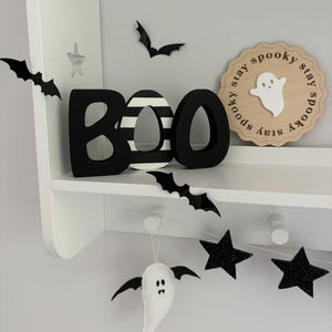 May include: Black and white wooden BOO letters with a black and white striped O, a white ghost with a black face, and a wooden sign that says "Stay spooky stay spooky stay spooky" with a white ghost in the center.