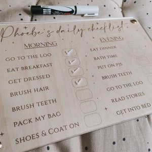 May include: A wooden checklist board with the text "Phoebe's daily checklist" and a list of morning and evening tasks. The board has checkboxes next to each task, and some of the boxes are checked off with white checkmarks.