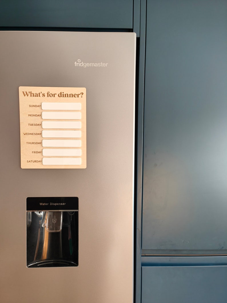 May include: A stainless steel refrigerator with a water dispenser and a magnetic meal planner that says "What's for dinner?" with spaces for each day of the week.