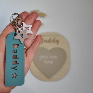 May include: A teal blue keychain with the word "Daddy" and a star cutout. The keychain has two small stars attached to it, one white and one pink.