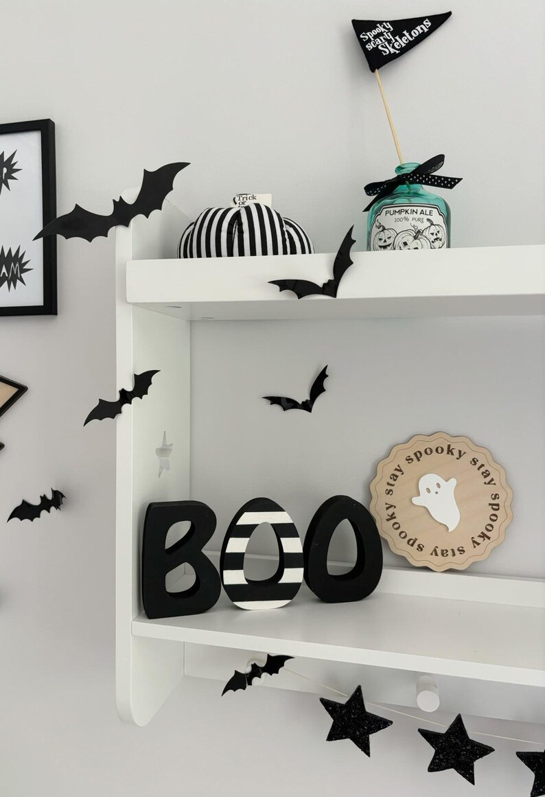 May include: Black and white striped BOO letters with a black and white striped pumpkin, a black and white ghost sign that says "stay spooky stay spooky stay spooky stay", and black bats on a white shelf.