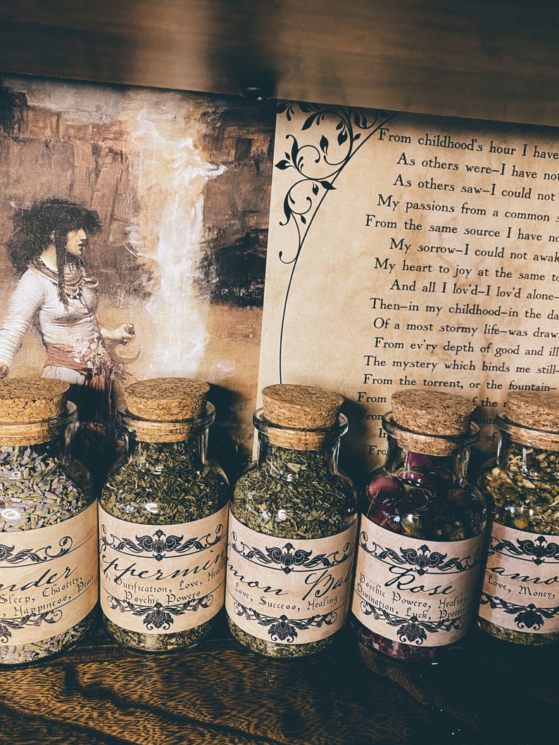 Puede incluir: Cinco peque&ntilde;os frascos de vidrio con tapas de corcho llenos de hierbas y flores secas. Cada frasco tiene una etiqueta con un nombre y una descripci&oacute;n diferentes. Las etiquetas son de estilo vintage con letras negras sobre fondo marr&oacute;n. Los frascos est&aacute;n sobre una superficie de madera. El texto en las etiquetas dice: "Order", "Peppermint", "Common Balm", "Rose", "Amon".