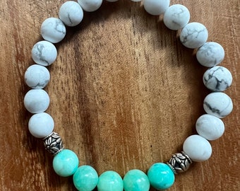 May include: A white and green beaded bracelet with silver accents. The bracelet is made of round beads and has a graduated color scheme, starting with white beads and transitioning to green beads.