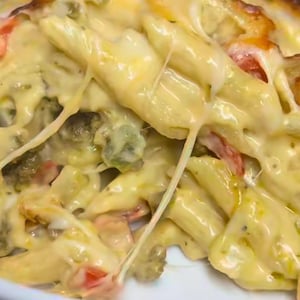 以下が含まれることがあります： ペンネ、ブロッコリー、トマトが入ったオーブン焼きパスタ料理のクローズアップ。溶けたチーズで覆われています。チーズは上部が黄金色で糸を引いており、ハーブとスパイスが見えます。白いボウルで提供されます。