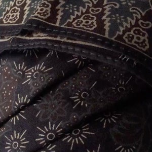 Puede incluir: Una tela marr&oacute;n oscura con un patr&oacute;n blanco de peque&ntilde;as estrellas y formas m&aacute;s grandes que se asemejan al sol. La tela tiene una superficie texturizada, ligeramente rugosa.