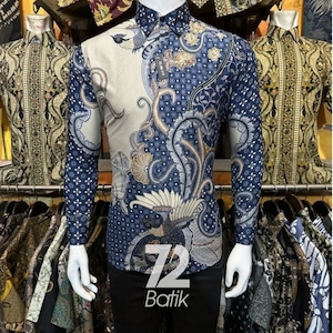 Puede incluir: Una camisa de manga larga con un diseño batik único. La camisa presenta una combinación de colores crema y azul marino con patrones intrincados. El texto "72 Batik" se muestra en la parte delantera de la camisa.