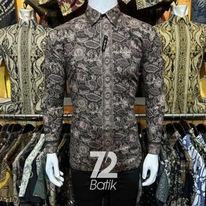 Può includere: Una camicia a maniche lunghe con un motivo floreale marrone e bianco. La camicia ha una chiusura con bottoni sul davanti e un colletto. La camicia è etichettata "72 Batik".