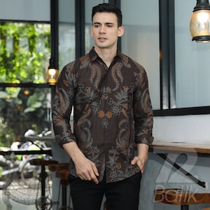 Puede incluir: Una camisa marrón de manga larga con un diseño estampado. El estampado presenta motivos florales y paisley marrones, naranjas y blancos.