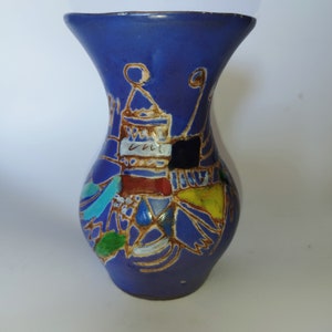 Puede incluir: Un pequeño jarrón de cerámica azul con un diseño caprichoso que presenta formas geométricas y líneas de colores. El jarrón está decorado con una variedad de colores, incluyendo azul, verde, amarillo, rojo y negro.