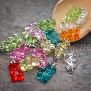 May include: A collection of translucent, gummy bear-shaped charms in various colors including red, pink, yellow, green, orange, and clear. Each small bear figure features a silver-toned metal jump ring attached to the top for hanging purposes.