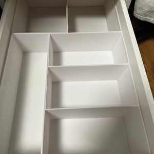 Peut inclure: Organiseur de tiroir blanc avec cinq compartiments. L'organisateur est en plastique et a une finition blanche lisse.