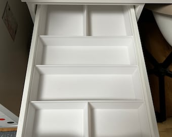 May include: A white desk with an open drawer, revealing several compartments. The drawer is divided into sections, perfect for organizing small items. Sewing supplies are visible on the desk surface above the drawer.