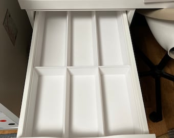 May include: A white desk drawer with a divided interior, perfect for organizing small items. The drawer is open, revealing six compartments. The desk surface above holds spools of thread in various colors, suggesting a sewing or crafting workspace.
