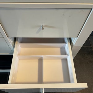 Könnte beinhalten: Eine weiße Schublade mit einem silbernen Griff ist geöffnet und zeigt einen weißen Organizer mit drei Fächern.