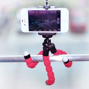 May include: A pink flexible tripod with a smartphone attached. The tripod has a black base and is wrapped in pink rubber. The smartphone is white and has a black screen.