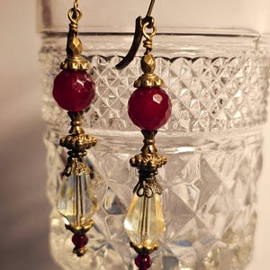 May include: A pair of dangle earrings with a red faceted gemstone, a clear faceted crystal, and gold-toned metal accents.