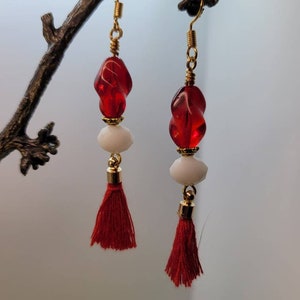 May include: Red and white dangle earrings with gold accents and red tassels.