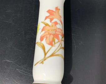 May include: A white ceramic vase with a gold rim and a floral design featuring pink lilies on a white background.
