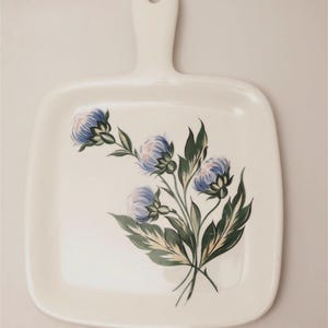 May include: A handmade wooden sign with the text "Welcome" in a handwritten style. The sign is painted white with a distressed finish, and a small green leaf is attached to the top. The sign measures approximately 12 inches wide.