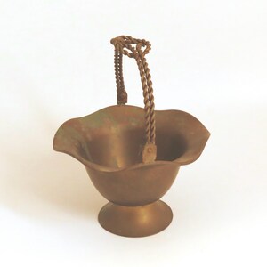 May include: A small, brass, decorative bowl with a twisted wire handle. The bowl has a scalloped edge and a pedestal base.