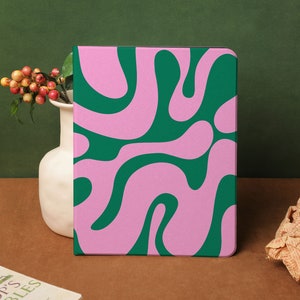 以下が含まれることがあります： ピンクとグリーンの模様の電子タブレット用のケース。ケースは、渦巻くラインでモダンな抽象的なデザインになっています。