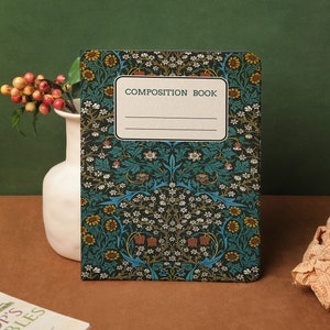 Puede incluir: Un cuaderno de composición con un estampado floral en verde azulado, amarillo y blanco. La portada presenta el texto "COMPOSITION BOOK" en una etiqueta rectangular. El cuaderno está colocado frente a un jarrón blanco con bayas.