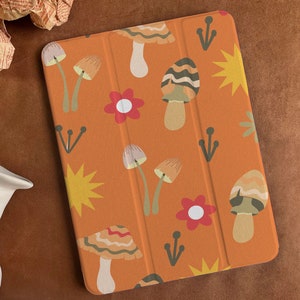 Könnte beinhalten: Orangefarbene iPad-Hülle mit einem sich wiederholenden Muster aus Pilzen, Blumen und Sternen. Die Pilze sind in Braun- und Weißtönen gehalten, die Blumen sind rot mit weißen Zentren und die Sterne sind gelb.