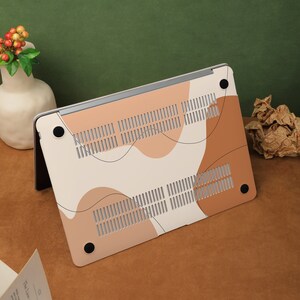 May include: A white laptop case with a brown and beige abstract design. The case has a textured surface and a black rubberized bottom.