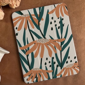 Könnte beinhalten: Eine weiße Tablethülle mit einem Blumenmuster. Die Hülle zeigt große orangefarbene Blumen mit dunkelgrünen Blättern und schwarzen Punkten auf weißem Hintergrund.