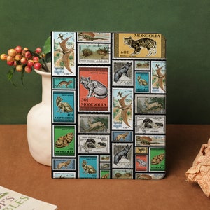 May include: A notebook cover featuring a collage of vintage postage stamps depicting animals, such as a cat, a fox, a deer, and a bird. The stamps are from Mongolia and display the text "MONGOLIA" in multiple languages.