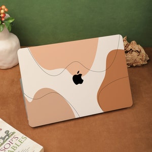 May include: A white laptop with a brown and beige abstract design on the cover. The Apple logo is visible in the center of the laptop.