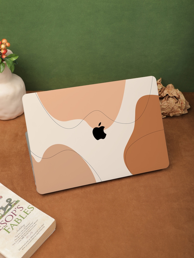 May include: A white laptop with a brown and beige abstract design on the cover. The Apple logo is visible in the center of the laptop.