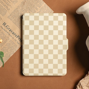 Peut inclure: Une liseuse à motifs de carreaux beiges et blancs avec une bordure noire. La liseuse est posée sur une surface brune.