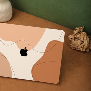 May include: A white laptop with an abstract design in shades of peach, brown, and cream. The laptop has an Apple logo on the lid.