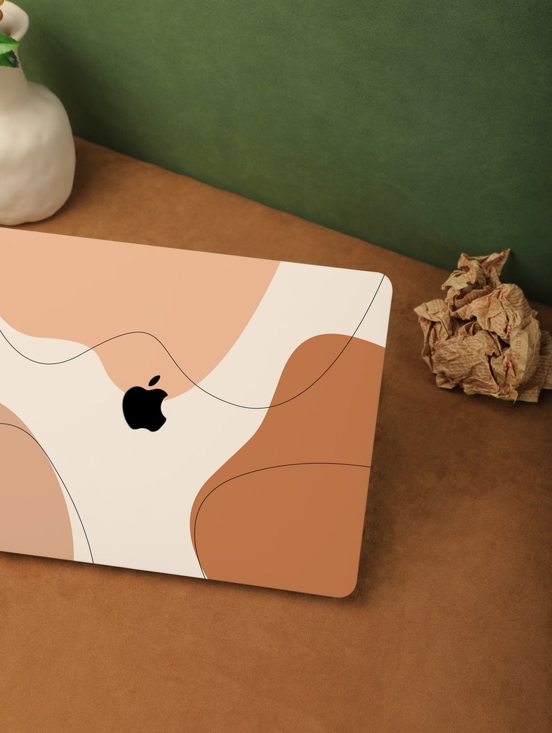 May include: A white laptop with an abstract design in shades of peach, brown, and cream. The laptop has an Apple logo on the lid.