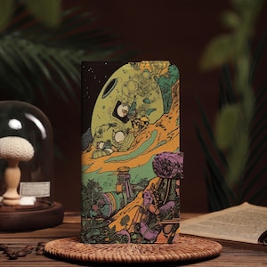 Puede incluir: Una funda de teléfono negra con una ilustración colorida de una nave espacial aterrizando en un planeta con un paisaje verde, amarillo y azul.