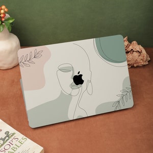 Könnte beinhalten: Eine Laptop-Haut mit minimalistischem Design, das eine Linienzeichnung eines Gesichts mit grünem und rosa Hintergrund zeigt. Das Apple-Logo ist auf dem Laptop sichtbar.