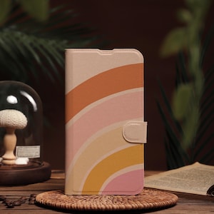 Könnte beinhalten: Eine rosa, orange und gelbe Handyhülle mit einem Regenbogenmuster. Die Hülle ist aus Leder und hat eine Klappe, die mit einem Druckknopf geschlossen wird.