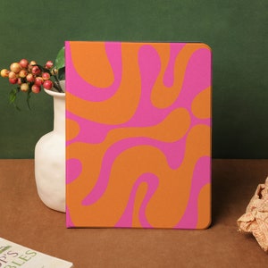 以下が含まれることがあります： オレンジとピンクの渦巻き模様の抽象的なパターンが施されたノートカバー