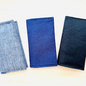 May include: Three fabric pouches in different colours: grey, blue, and black. The pouches are made of a textured fabric and have a simple, rectangular shape.