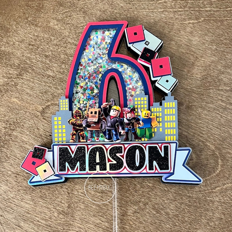May include: A red, blue, and black cake topper with a glittery number six, a cityscape, and the name "MASON" in black letters. The cake topper features characters from the popular online game Roblox.