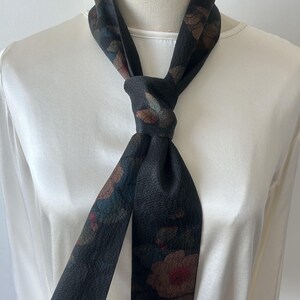 May include: A black silk scarf with a floral print. The scarf is tied around the neck in a knot.