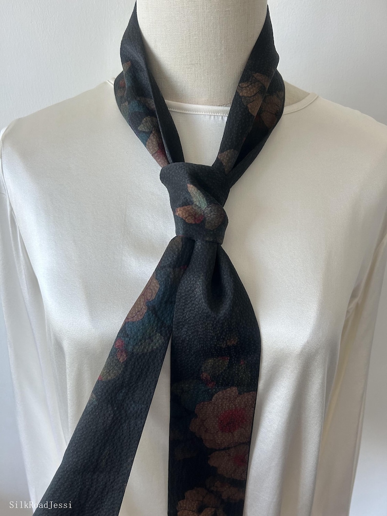 May include: A black silk scarf with a floral print. The scarf is tied around the neck in a knot.