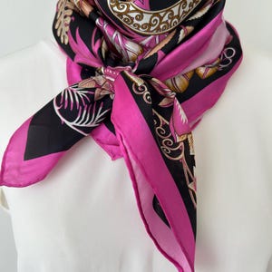 May include: A square silk scarf with a vibrant floral design. The scarf features a bold color palette of black, hot pink, and gold. The scarf is knotted around a neck, showcasing the intricate patterns and luxurious texture.