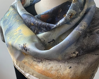 May include: A light blue, beige, and brown silk scarf with a watercolor-like design of birds and abstract shapes. The scarf is folded and draped around a mannequin's neck.