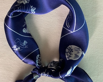 May include: A blue silk scarf with a white floral pattern. The scarf is tied in a knot and the ends are hanging down.