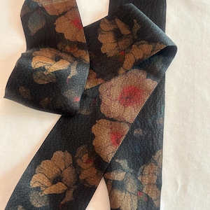 May include: A black fabric ribbon with a floral pattern in shades of brown, red, and green. The flowers are stylized and have a textured appearance.