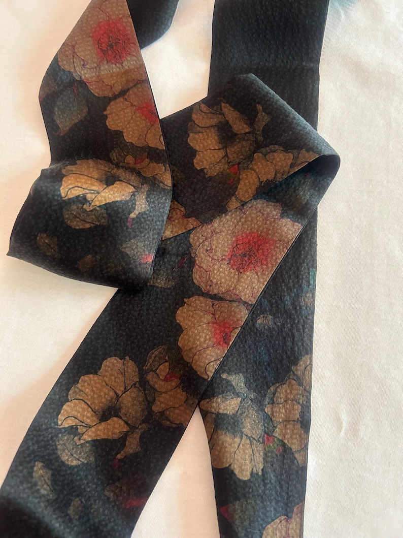 May include: A black fabric ribbon with a floral pattern in shades of brown, red, and green. The flowers are stylized and have a textured appearance.