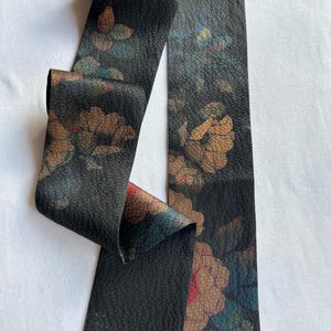 May include: A black fabric ribbon with a floral pattern in shades of brown, blue, and pink. The ribbon has a textured surface and is approximately 1.5 inches wide.