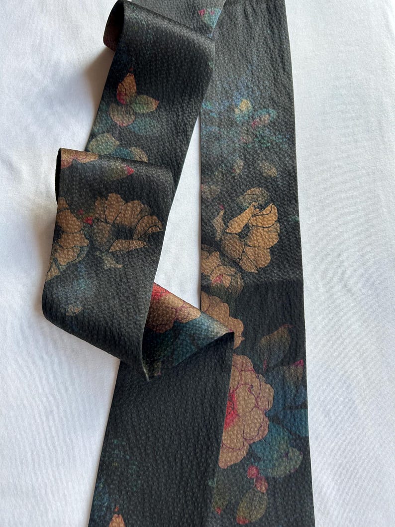 May include: A black fabric ribbon with a floral pattern in shades of brown, blue, and pink. The ribbon has a textured surface and is approximately 1.5 inches wide.